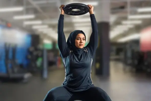 Woman lifting weighted plate above head | Reps vs Sets | G oFit Blog