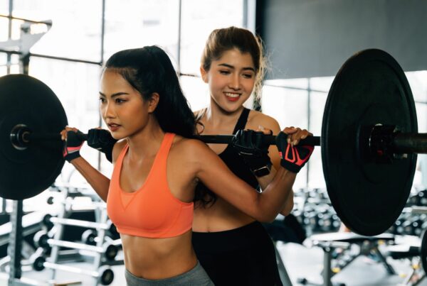 A female personal trainer assisting someone with barbells in a squat