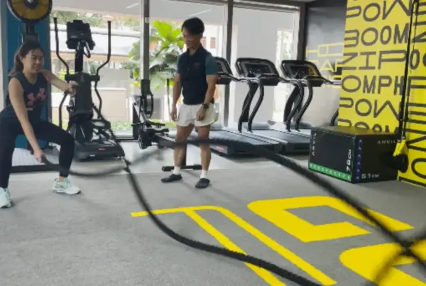 A woman using battle ropes while a personal trainer looks on